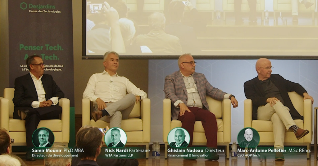 quatre hommes sur un podium assis dans des fauteuils sont présenté pour un panel de discussion sur le financement des projets de AI et IoT.